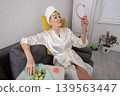 Elderly woman relaxes with pieces of cucumber on her face, looking in the mirror at home during self -service 139563447