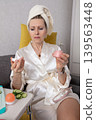An elderly woman in a dressing gown, performing a routine of skin care at home with cucumber slices and preparing a face mask 139563448