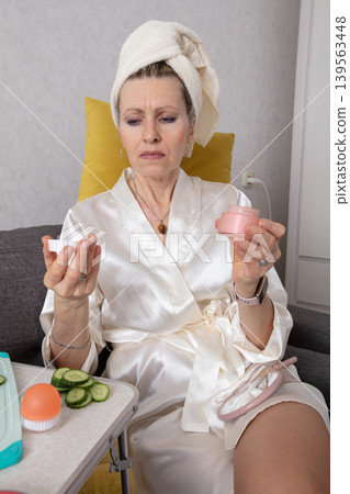 An elderly woman in a dressing gown, performing a routine of skin care at home with cucumber slices and preparing a face mask 139563448
