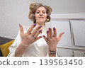 Senior woman showcasing meticulous nail art in a cozy indoor setting during the afternoon 139563450