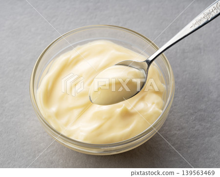 Creamy mayonnaise scooped from a glass bowl with a spoon against a gray background. Creamy mayonnaise scooped from a glass bowl with a spoon against a gray background. 139563469