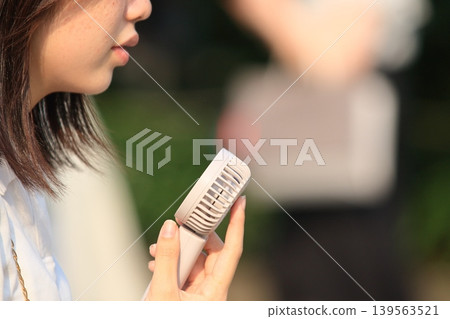 A woman walking with a handheld fan 139563521