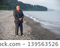A man in an official suit, standing barefoot on the beach Banner early in the morning in a calm Primorsky place 139563526