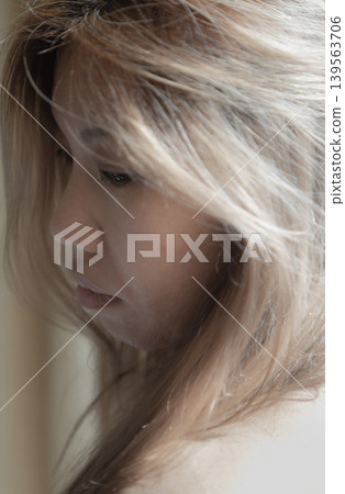 Enveloped in soft light, the woman downward gaze and the delicate sweep of her golden hair create a portrait of grace and enduring melancholy. Enveloped in soft light, the woman downward gaze and the delicate sweep of her golden hair create a portrait of grace and enduring melancholy. 139563706