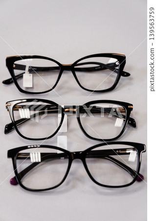 Three black stylish eyeglasses frames arranged vertically on white background with reflections close up shot Three black stylish eyeglasses frames arranged vertically on white background with reflections close up shot 139563759