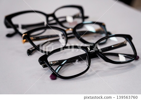 Selective focus black eyeglasses frames arranged on white table surface, optical vision accessory closeup, minimalist composition Selective focus black eyeglasses frames arranged on white table surface, optical vision accessory closeup, minimalist composition 139563760