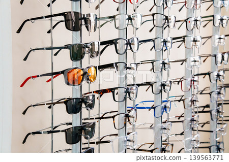 Display of eyeglasses and sunglasses for sale at optical store with colorful frames on metal rack 139563771