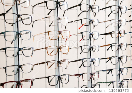 Multiple pairs of eyeglasses displayed on a white rack for sale at an optical shop with colorful frames Multiple pairs of eyeglasses displayed on a white rack for sale at an optical shop with colorful frames 139563773