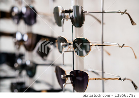 Collection of fashionable sunglasses displayed on white metal rack for retail store window showcase with different frame colors Collection of fashionable sunglasses displayed on white metal rack for retail store window showcase with different frame colors 139563782