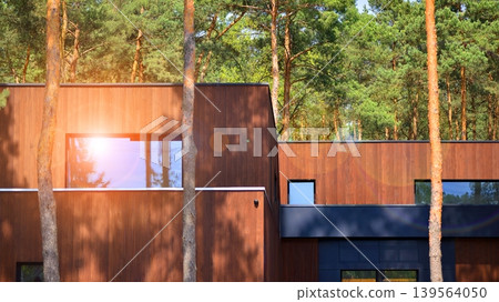 Villa surrounded by trees on bright sunny day. Beautiful exterior of modern luxury home with linear design and elegant use of wood and metal. Villa surrounded by trees on bright sunny day. Beautiful exterior of modern luxury home with linear design and elegant use of wood and metal. 139564050
