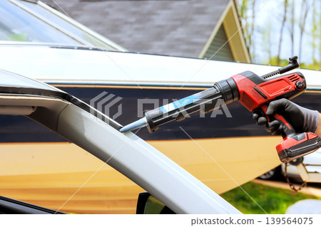 Hand using tool to apply sealant on car near boat Hand using tool to apply sealant on car near boat 139564075