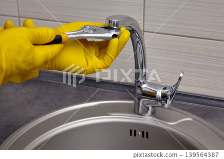 repairing a kitchen sink faucet with gloves and a wrench repairing a kitchen sink faucet with gloves and a wrench 139564387