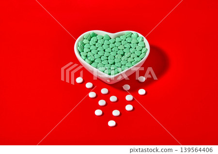 turquoise heart-shaped cardiology pills in a ceramic bowl on a red background. 139564406