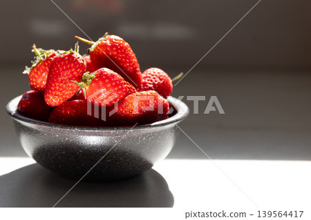 Fresh red strawberries in black bowl on white surface. Juicy fruit still life with soft natural daylight lighting. Healthy eating and summer freshness concept for dietary nutrition imagery. Fresh red strawberries in black bowl on white surface. Juicy fruit still life with soft natural daylight lighting. Healthy eating and summer freshness concept for dietary nutrition imagery. 139564417