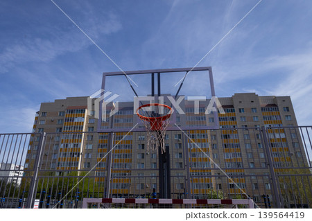 Basketball hoop mounted on pole next to urban apartment building. Accessible outdoor sports facility in residential neighborhood Basketball hoop mounted on pole next to urban apartment building. Accessible outdoor sports facility in residential neighborhood 139564419