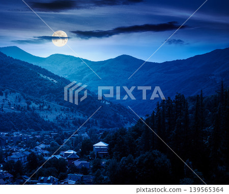 carpathian mountain landscape on summer night. full moon over view in to the valley of town near forested hill of mountain range. mysterious travel background of alpine countryside carpathian mountain landscape on summer night. full moon over view in to the valley of town near forested hill of mountain range. mysterious travel background of alpine countryside 139565364