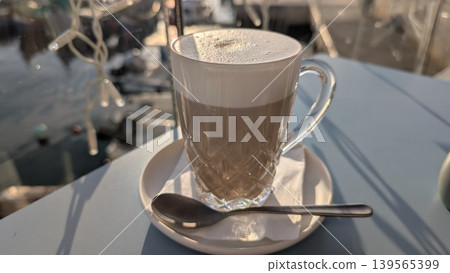 Cappuccino with a thick layer of foam in a glass cup on the table at harbor Cappuccino with a thick layer of foam in a glass cup on the table at harbor 139565399
