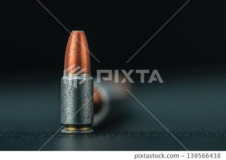 Copper and silver bullet stands upright on a dark, textured surface 139566438