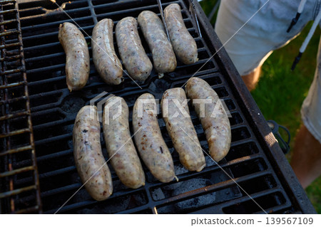 Several sausages cook on a grill grate over charcoal outdoors Several sausages cook on a grill grate over charcoal outdoors 139567109