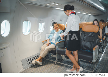 Senior woman receiving in flight service from flight attendant in business class airplane seat 139567561