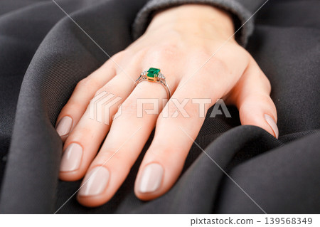 Beautiful female hand with gold ring with diamonds and emerald on gray background Beautiful female hand with gold ring with diamonds and emerald on gray background 139568349