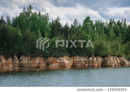 Scenic forest view with cliff and lake under cloudy sky Scenic forest view with cliff and lake under cloudy sky 139568955