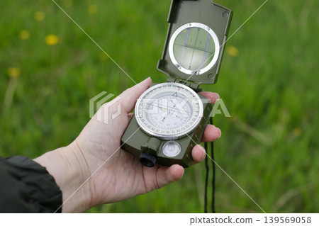 Woman's hand holding a opened compass for orientation against a background of green grass. Travel and navigation 139569058