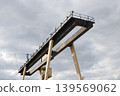 Industrial gantry crane structure against a dramatic cloudy sky, viewed from below with weathered metal beams and operator cabin 139569062