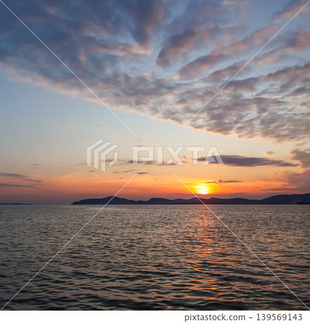 Sun setting over the calm sea reflecting orange and red light, creating a peaceful and serene natural landscape Sun setting over the calm sea reflecting orange and red light, creating a peaceful and serene natural landscape 139569143