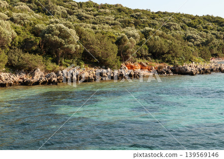 Turquoise water reaching the rocky shoreline of Bitez, Bodrum, Turkey, with abundant green vegetation covering the hills Turquoise water reaching the rocky shoreline of Bitez, Bodrum, Turkey, with abundant green vegetation covering the hills 139569146