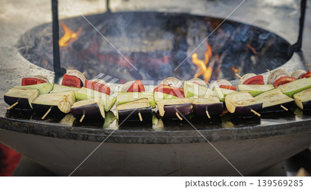 Vegetable skewers with eggplant, zucchini, pepper, mushroom cook on grill, flame and smoke. Concept of vegetable barbecue for catering, picnic, vegan menu, street food, summer party, outdoor cooking 139569285