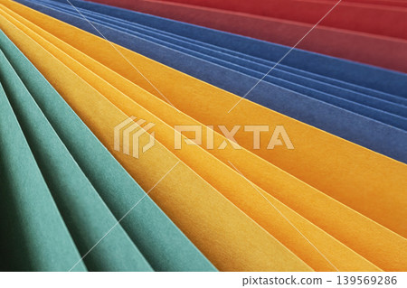 Color paper sheets form diagonal layered stripes in teal, yellow, orange, blue, red tones. Natural background with paper texture for design, craft, education, color layout, copy space 139569286
