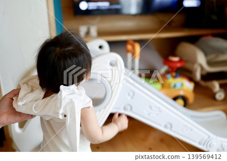 A one-year-old girl's back as her parent helps her get dressed. A one-year-old girl's back as her parent helps her get dressed. 139569412