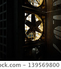 Metal ventilation fans lit by window, rusted grille and shafts creating deep shadows and textured beams, vintage machinery visible through grid, gritty 139569800