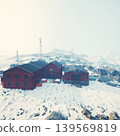 Nestled in a serene winter landscape, this remote lodge boasts red wooden structures amid vast snow covered terrain. Communication towers stand tall in the distance, enhancing its isolation. 139569819