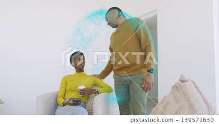 Sitting woman in yellow top, standing man in mustard sweater leaning in living room, holding phone Sitting woman in yellow top, standing man in mustard sweater leaning in living room, holding phone 139571630