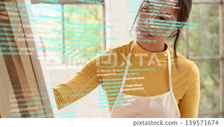 Reaching woman wearing mustard turtleneck and apron tracing code overlay on pane at home studio Reaching woman wearing mustard turtleneck and apron tracing code overlay on pane at home studio 139571674