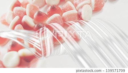 Glistening red-white gummies resting on white surface with curved clear strands and sugar crystals Glistening red-white gummies resting on white surface with curved clear strands and sugar crystals 139571709