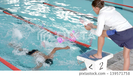 Crouching coach in hoodie timing swimmer splashing on block 2 at pool with stopwatch, copy space Crouching coach in hoodie timing swimmer splashing on block 2 at pool with stopwatch, copy space 139571758