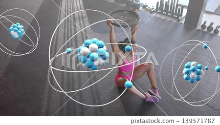 Pressing woman in pink workout gear holding weight plate overhead on gym floor, with orbit graphics Pressing woman in pink workout gear holding weight plate overhead on gym floor, with orbit graphics 139571787