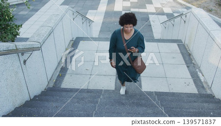 Climbing woman in teal dress ascending concrete steps to tiled plaza, holding phone and brown bag Climbing woman in teal dress ascending concrete steps to tiled plaza, holding phone and brown bag 139571837