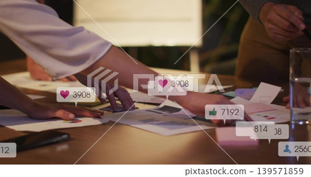 Pointing colleagues leaning over wooden table, reviewing charts with social overlays, satin top Pointing colleagues leaning over wooden table, reviewing charts with social overlays, satin top 139571859