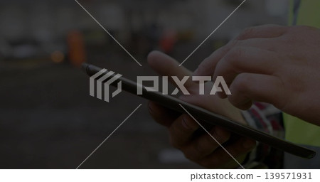 Tapping mid adult worker in safety vest, using tablet at work site, plaid sleeve visible Tapping mid adult worker in safety vest, using tablet at work site, plaid sleeve visible 139571931