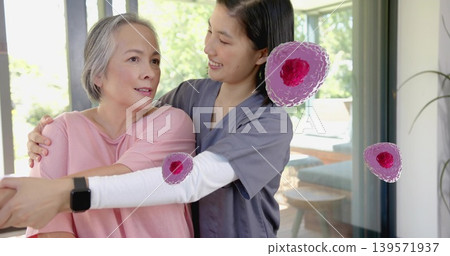 Guiding carer in gray scrubs helping senior in pink top raising arms home smartwatch pink dots Guiding carer in gray scrubs helping senior in pink top raising arms home smartwatch pink dots 139571937