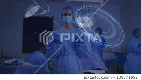 Standing central masked gowned clinician raising gloved hands in OR, projecting holographic UI 139571952