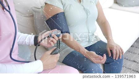 Measuring nurse in pink scrubs applying cuff to patient in green top and jeans at home Measuring nurse in pink scrubs applying cuff to patient in green top and jeans at home 139571963