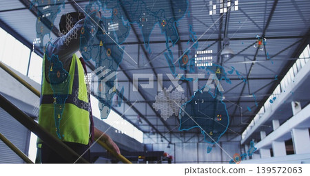 Interacting worker wearing yellow safety vest pointing at hologram world map on stair, copy space Interacting worker wearing yellow safety vest pointing at hologram world map on stair, copy space 139572063