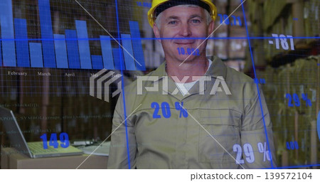 Standing warehouse lead in yellow hard hat and khaki shirt using laptop with blue data overlay Standing warehouse lead in yellow hard hat and khaki shirt using laptop with blue data overlay 139572104