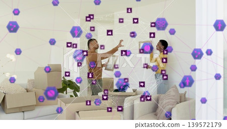 Standing brown-shirted man, yellow-top woman discussing move at home, tablet, boxes, purple overlay Standing brown-shirted man, yellow-top woman discussing move at home, tablet, boxes, purple overlay 139572179