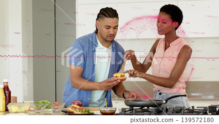 Assembling couple wearing casual shirts and jeans holding bun and spooning sauce in home kitchen Assembling couple wearing casual shirts and jeans holding bun and spooning sauce in home kitchen 139572180